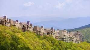 Eine Reihe von mehrstöckigen Gebäuden mit Balkonen, vor einer Kulisse aus grünen Hügeln und Bergen.