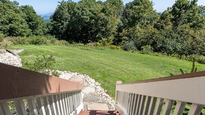 Eine Holzterrasse mit weißen Geländern, die zu einer grünen Fläche mit Bäumen im Hintergrund führt.