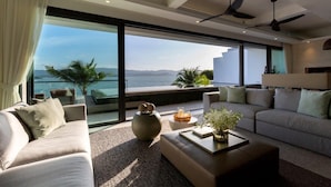 A modern living room with a large window overlooking a scenic view. There are two sofas, a coffee table, and a decorative vase. - Muscat 3-Bedroom Villa with Beach Access (Koh Samui)