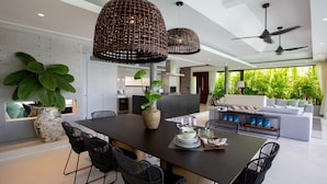 A modern kitchen with a dining area, featuring a large island, black chairs, and hanging wicker pendant lights. - Muscat 3-Bedroom Villa with Beach Access (Koh Samui)