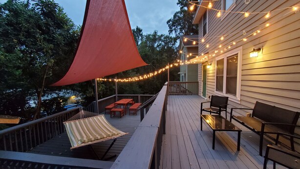 Um deck de madeira com móveis de exterior, luzes de corda e um toldo vermelho.
