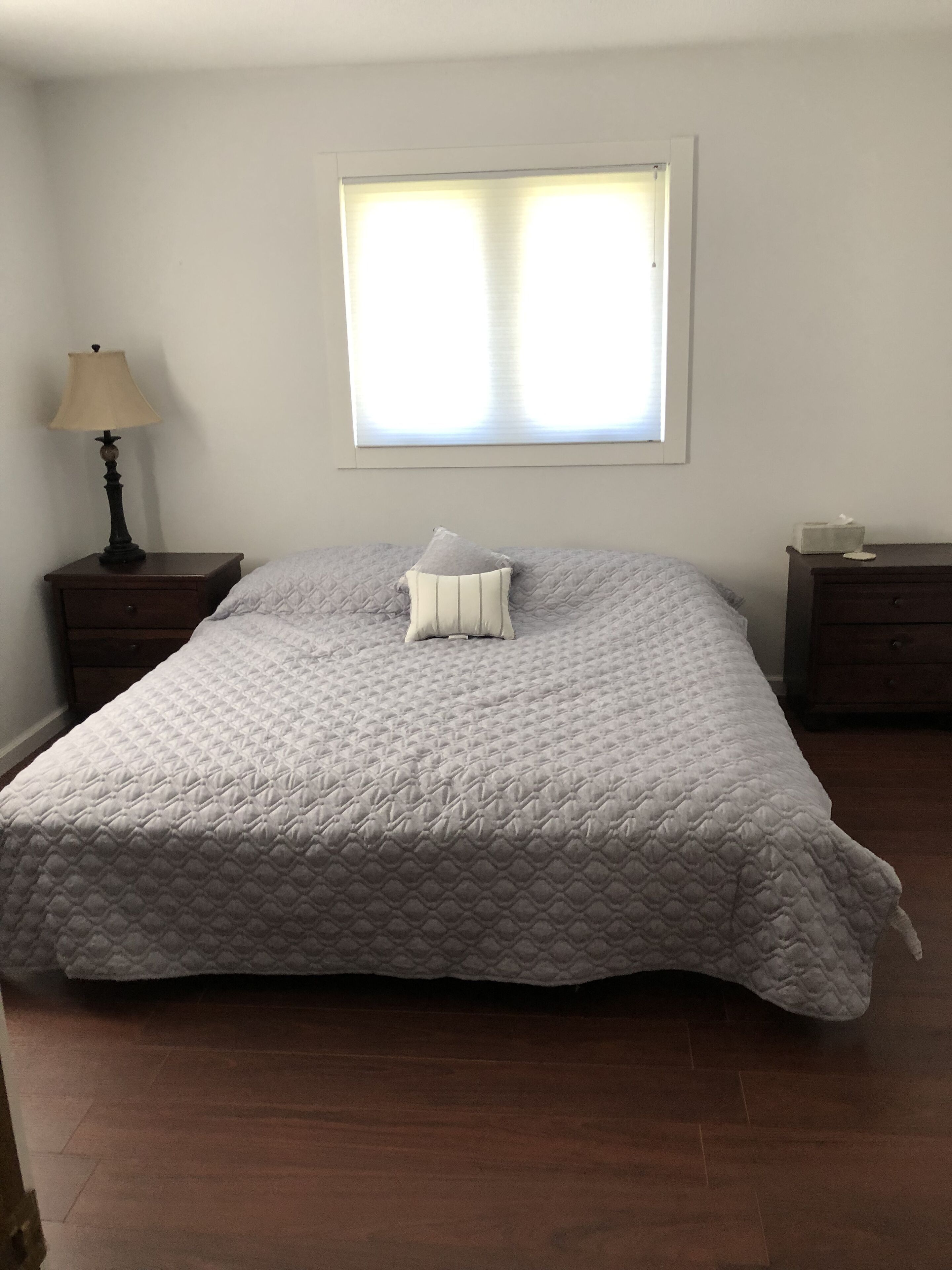 Ein Schlafzimmer mit einem Bett, einem Nachttisch mit Lampe, einem Fenster und einer Kommode.