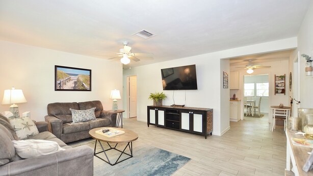 A living room with a sofa, coffee table, and a TV mounted on the wall. - Driftwood Way~ No Checkout Chores (Jensen Beach)