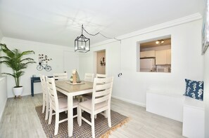 A dining area with a wooden table and chairs, a hanging light fixture, and a potted plant.