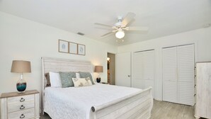 A bedroom with a large bed, two bedside tables, a ceiling fan, and white closets. - Driftwood Way~ No Checkout Chores (Jensen Beach)