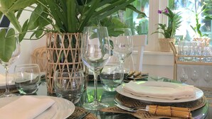 A round glass table set with white plates, folded napkins, and clear wine glasses.