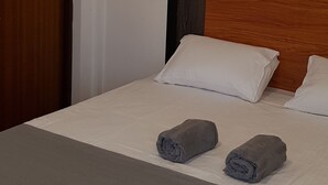 A neatly made bed with two rolled towels, a wooden headboard, and a framed picture on the wall. - Hotel Coldworld (Nuwara Eliya)