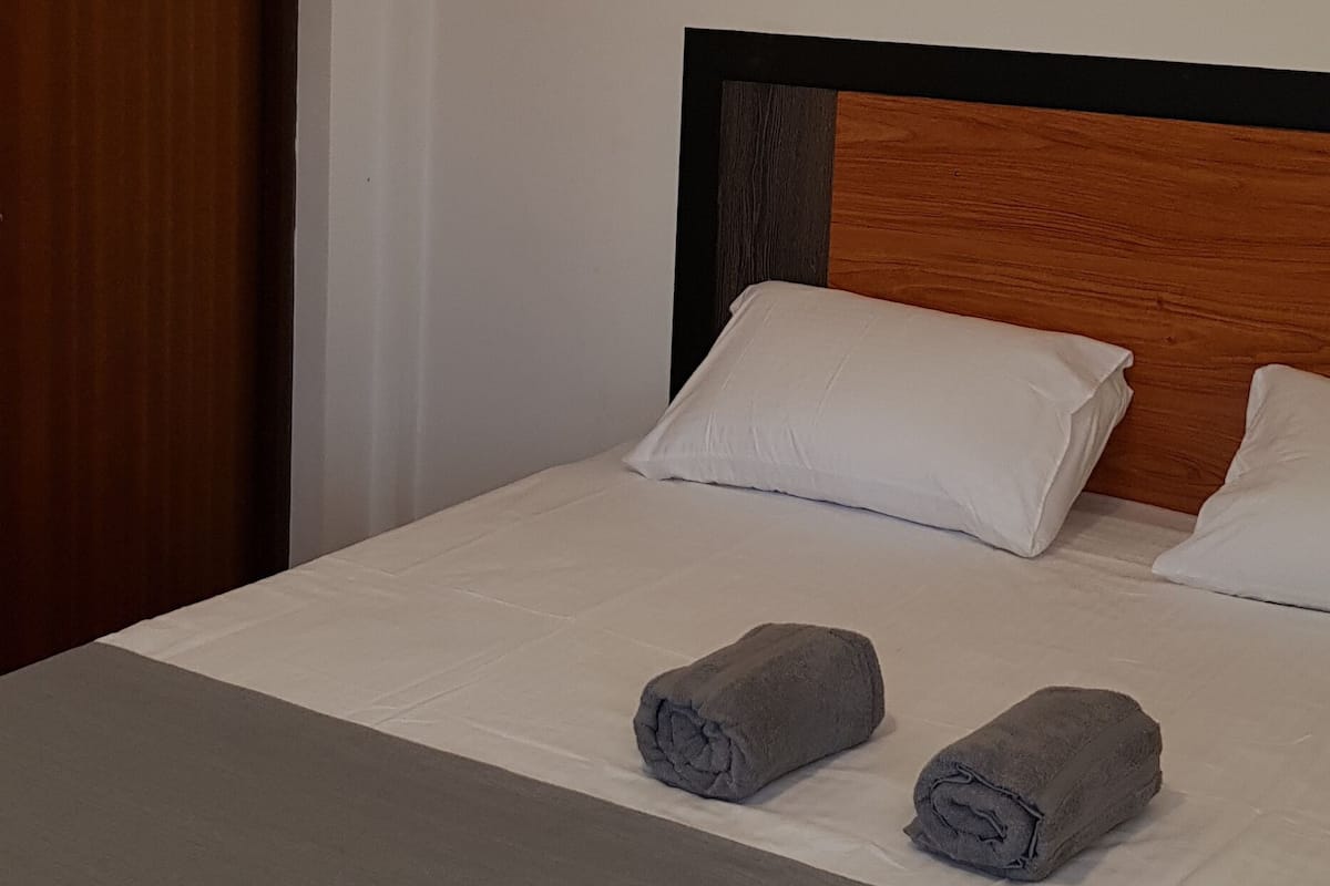 A neatly made bed with two rolled towels, a wooden headboard, and a framed picture on the wall.