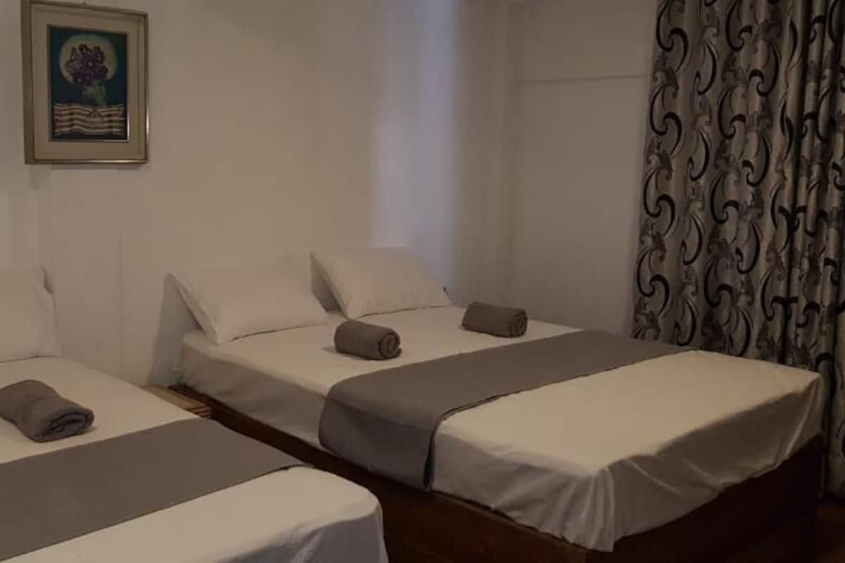 A hotel room with two single beds, each with a grey bedspread and pillows, and a framed picture on the wall.