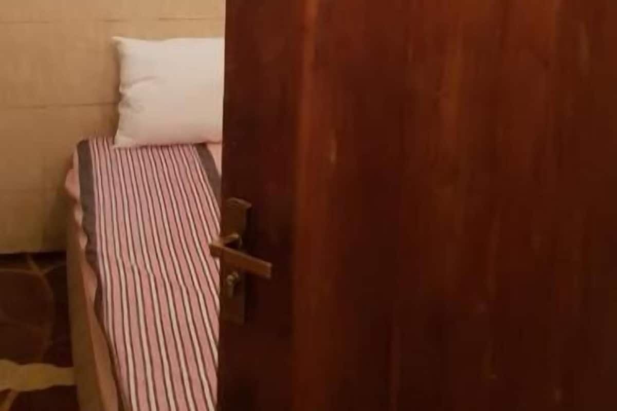 A wooden door with a number plate, a bed with striped bedding, and a wall with a tiled lower section.