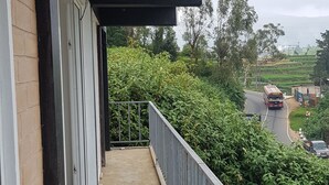 A balcony with a concrete floor, metal railing, and a view of a road with a bus. - Hotel Coldworld (Nuwara Eliya)