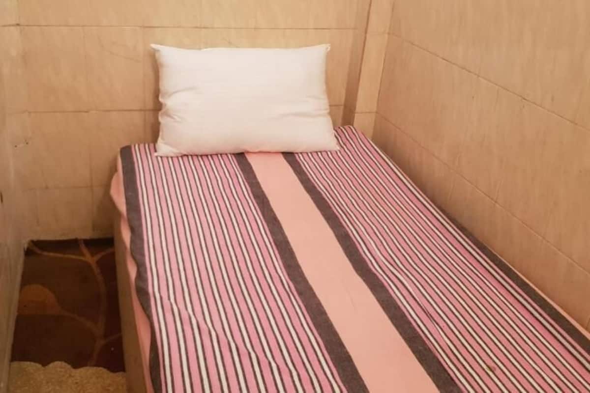 A small, narrow room with a single bed, a white pillow, and a striped bedspread.