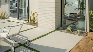Uma casa moderna com uma grande porta de vidro, um pátio com um carrinho e um jardim bem cuidado.