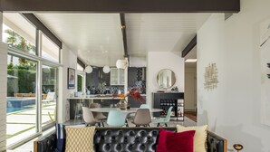 Uma sala de estar moderna com um sofá de couro preto, uma área de jantar com mesa de vidro e uma cozinha com uma ilha grande.