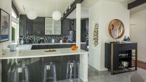 Uma cozinha moderna com uma ilha branca, banquetas de bar e um console de madeira escura com copos.