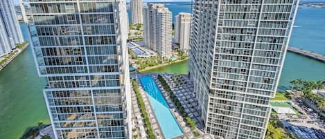 A high-rise building with a swimming pool and a marina in the background.