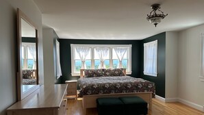 Une chambre à coucher comprenant un lit, une commode, un banc et de grandes fenêtres avec des rideaux.