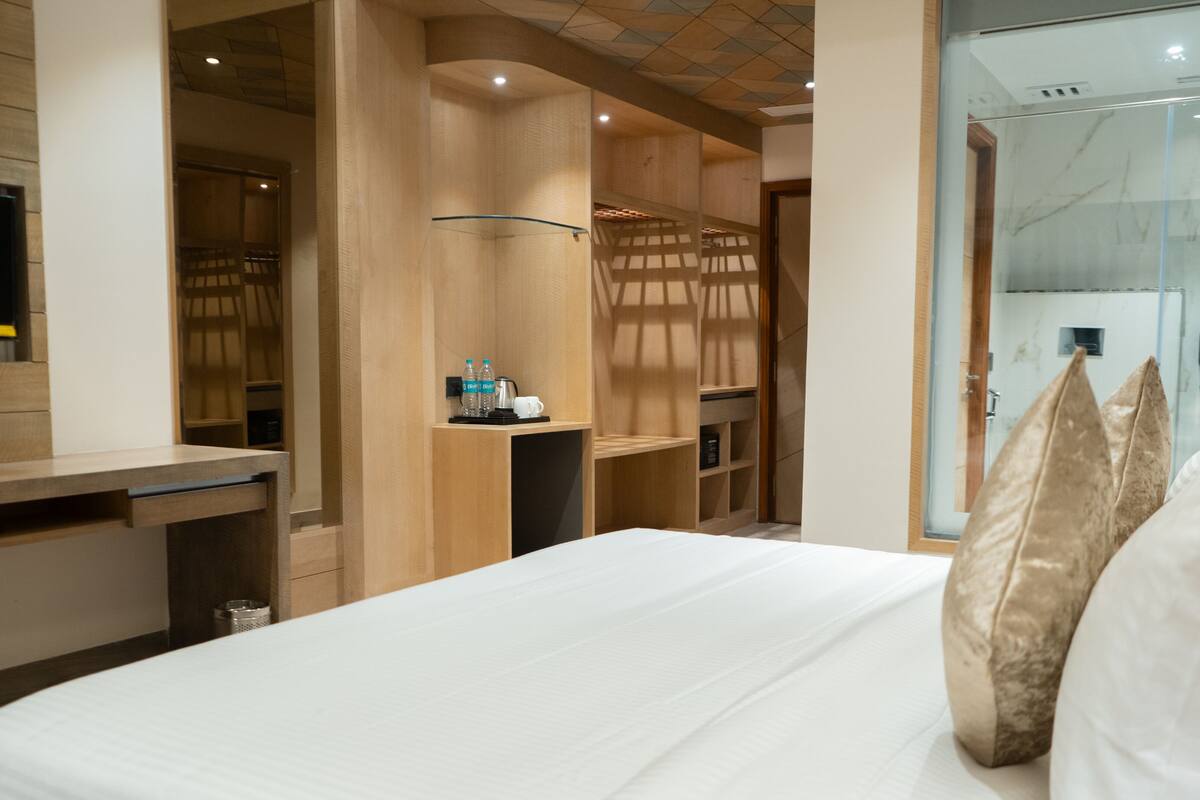 A modern hotel room with a large bed, a TV, a desk, and a shower area.