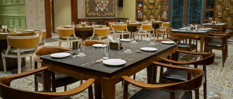 Een restaurant met meerdere tafels gedekt voor diners, met houten stoelen en een vloer met een patroon.