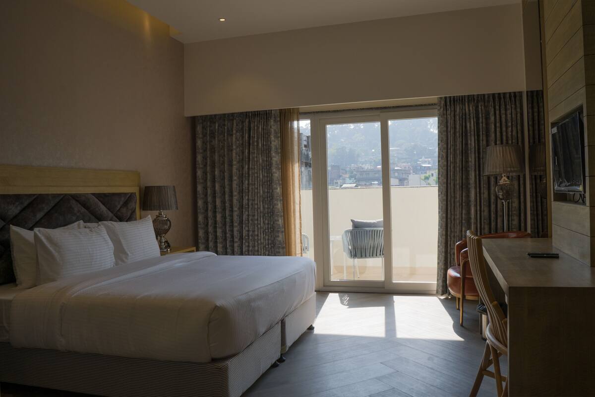 A hotel room with a bed, a desk, a chair, and a view through a glass door.
