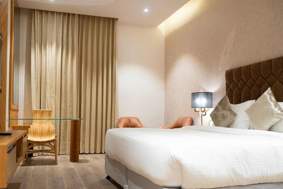 A hotel room with a bed, a desk, a chair, a lamp, and a curtain.