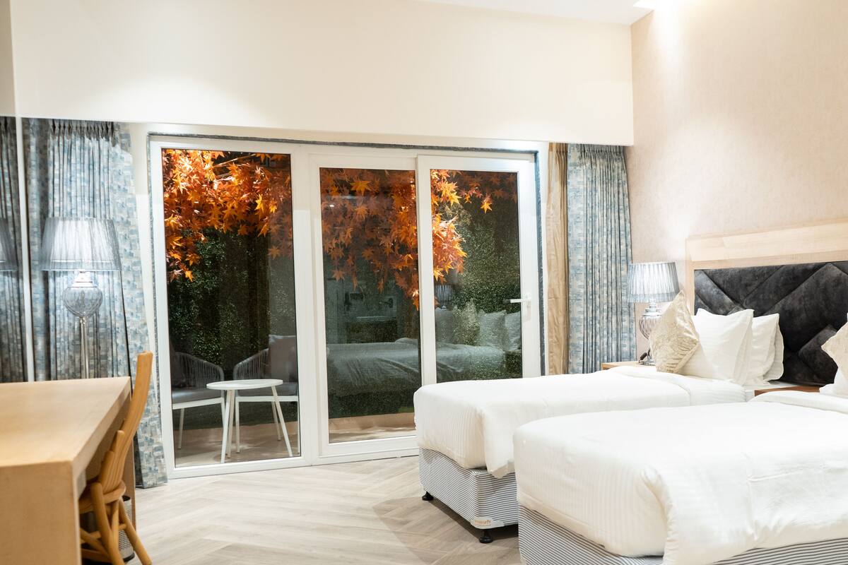 A hotel room with a bed, a desk, and a view of autumn leaves through the glass door.