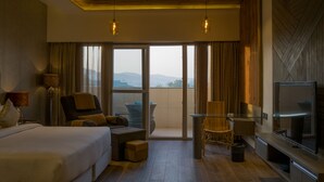 Habitación de hotel con cama, sofá, televisión y balcón con vistas a las montañas.