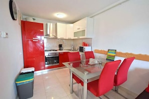 A compact kitchen with white and red cabinets, a glass dining table, and a trash bin.