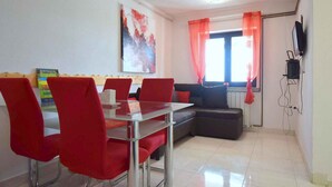 Un coin repas avec une table en verre et des chaises rouges, un canapé et un téléviseur fixé au mur.