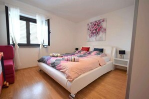 Une chambre Ă coucher avec un lit, une fenĂȘtre avec des rideaux, un tableau au mur et une chaise rouge.