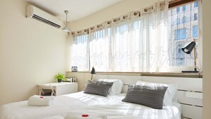 Habitación de hotel con dos camas, un escritorio, una silla, aire acondicionado, una ventana con cortinas y una lámpara.