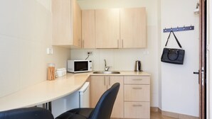 Cocina compacta con microondas, fregadero y cafetera. Hay una silla y un bolso colgando de un gancho.