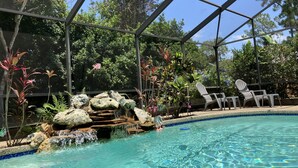 A pool with a waterfall feature surrounded by rocks and tropical plants.