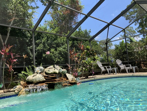 A pool with a waterfall feature surrounded by rocks and tropical plants.