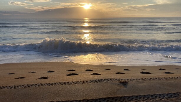 A beach with footprints leading to the water, waves, and a sunset over the ocean.