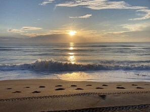 A beach with footprints leading to the water, waves, and a sunset over the ocean.