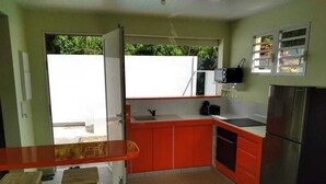 Cocina compacta con armarios rojos, un refrigerador de acero inoxidable y una pequeña barra con taburetes.