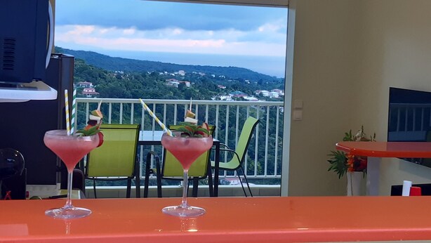 Un balcón con dos sillas y una mesa, un televisor y vistas de un paisaje montañoso.