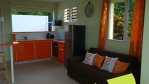 Una cocina compacta con área de comedor, un sofá con cojines decorativos y una ventana con cortinas.