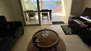Una sala de estar con vista a una masa de agua, un comedor con mesa y sillas, y un piano.