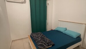 Una habitación pequeña con cama individual, cabecera blanca, cortina verde y colchón azul.