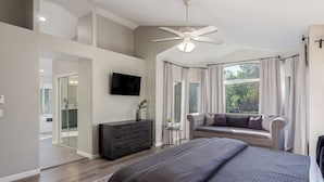Um quarto moderno com uma cama grande, uma cômoda escura, uma TV na parede e um ventilador de teto.