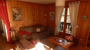 A wooden-floored living room with a sofa, a small table, and a window with curtains.
