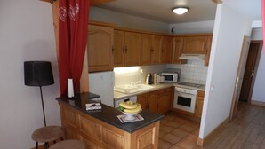 A compact kitchen with wooden cabinets, a microwave, a stove, and a small bar area with stools.
