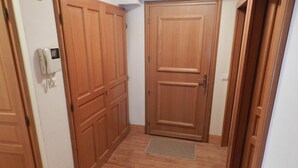 A hallway with wooden doors, a doormat, and a wall-mounted intercom.
