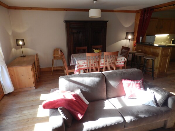 A cozy living area with a sofa, wooden dining table, chairs, and a kitchen area.