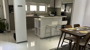 Une cuisine moderne avec des meubles blancs, un îlot central doté de tabourets et un coin repas avec une table et des chaises en bois.