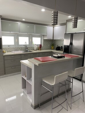Una cocina moderna con una isla central, taburetes de bar y electrodomésticos de acero inoxidable.