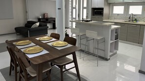 Une cuisine moderne dotée d’un îlot central, de tabourets de bar blancs et d’une table à manger agrémentée d’assiettes dorées.
