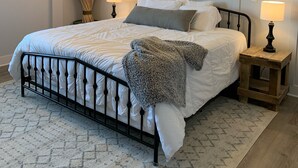 Un dormitorio ordenado con cama, lámparas de noche, ventilador de techo y un cuadro en la pared.